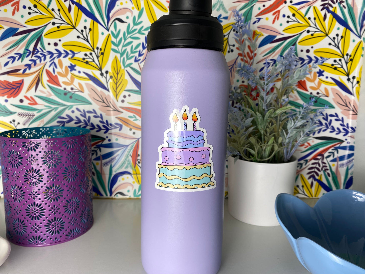 Purple water bottle with a cake and candles sticker on a colorful floral background