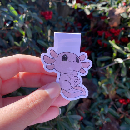 Hand holding a pink axolotl magnetic bookmark in front of green foliage with red berries