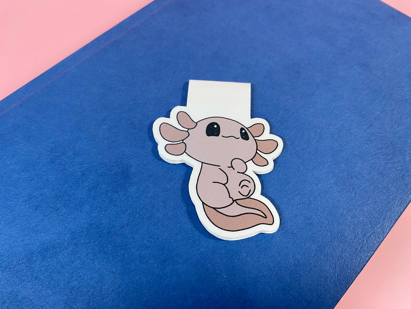 Cute axolotl magnetic bookmark on a blue surface with a pink border