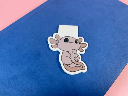 Cute axolotl magnetic bookmark on a blue surface with a pink border