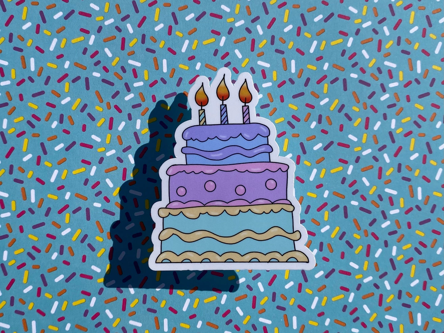 Sticker of a birthday cake with candles on a background of colorful sprinkles