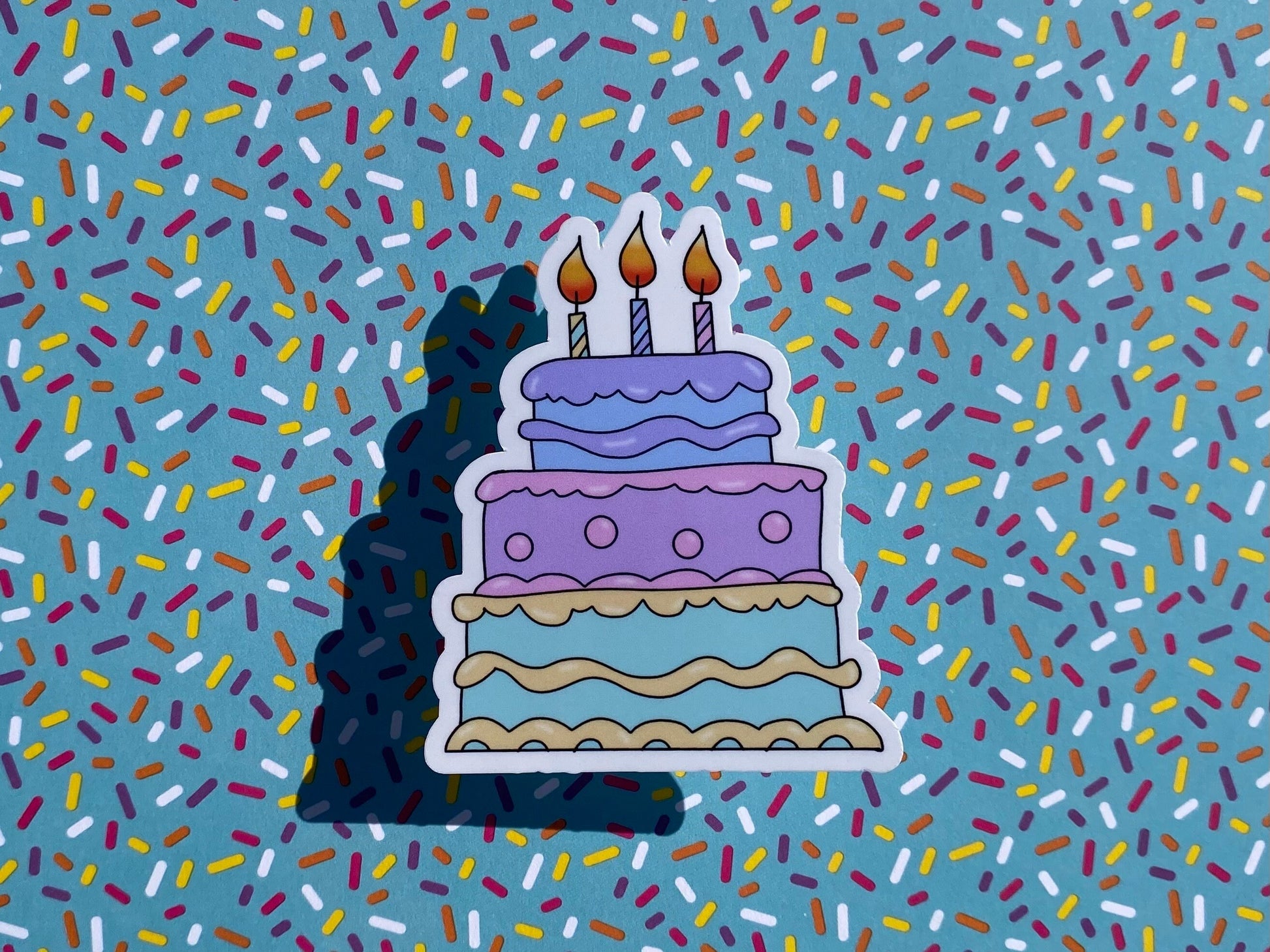 Sticker of a birthday cake with candles on a background of colorful sprinkles
