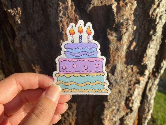 Sticker of a birthday cake with candles held against a tree trunk.