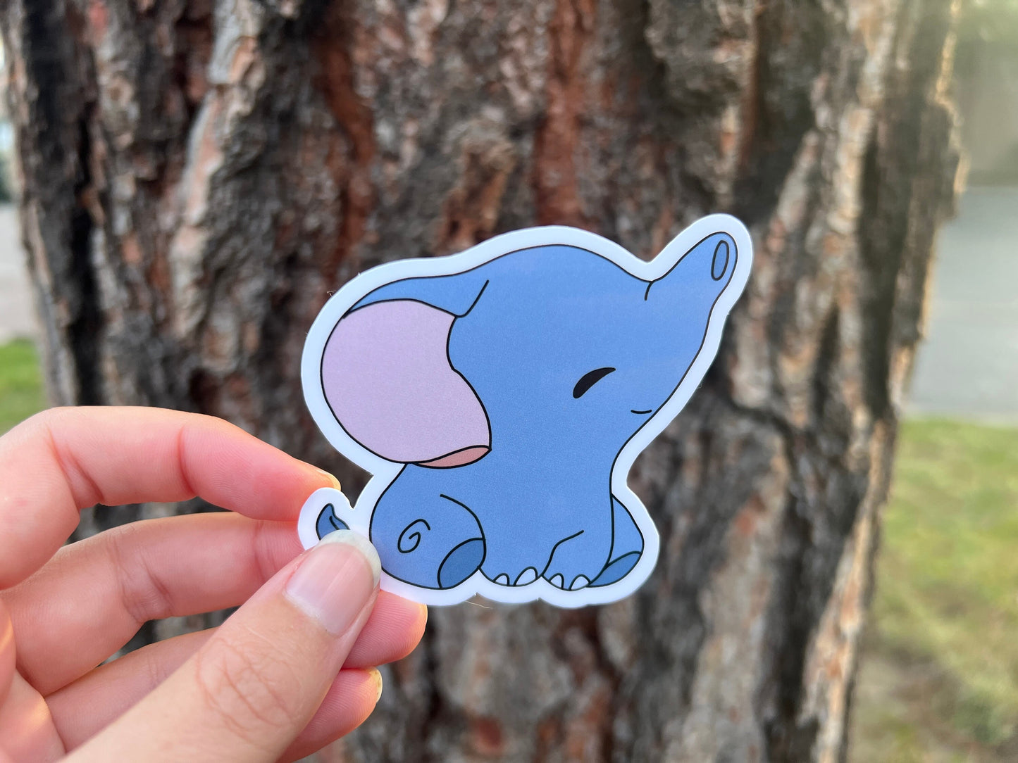 Hand holding a blue elephant sticker in front of a tree