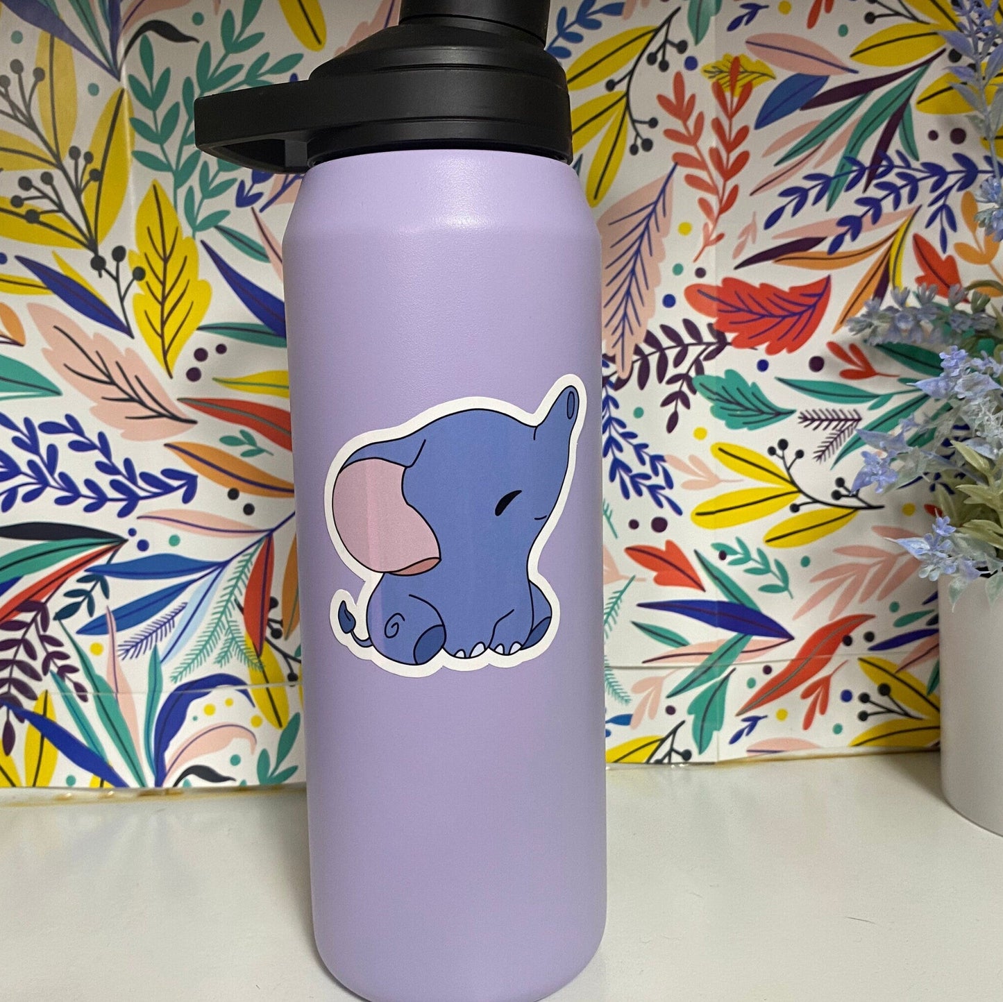 Purple water bottle with a cartoon elephant sticker against a colorful floral background