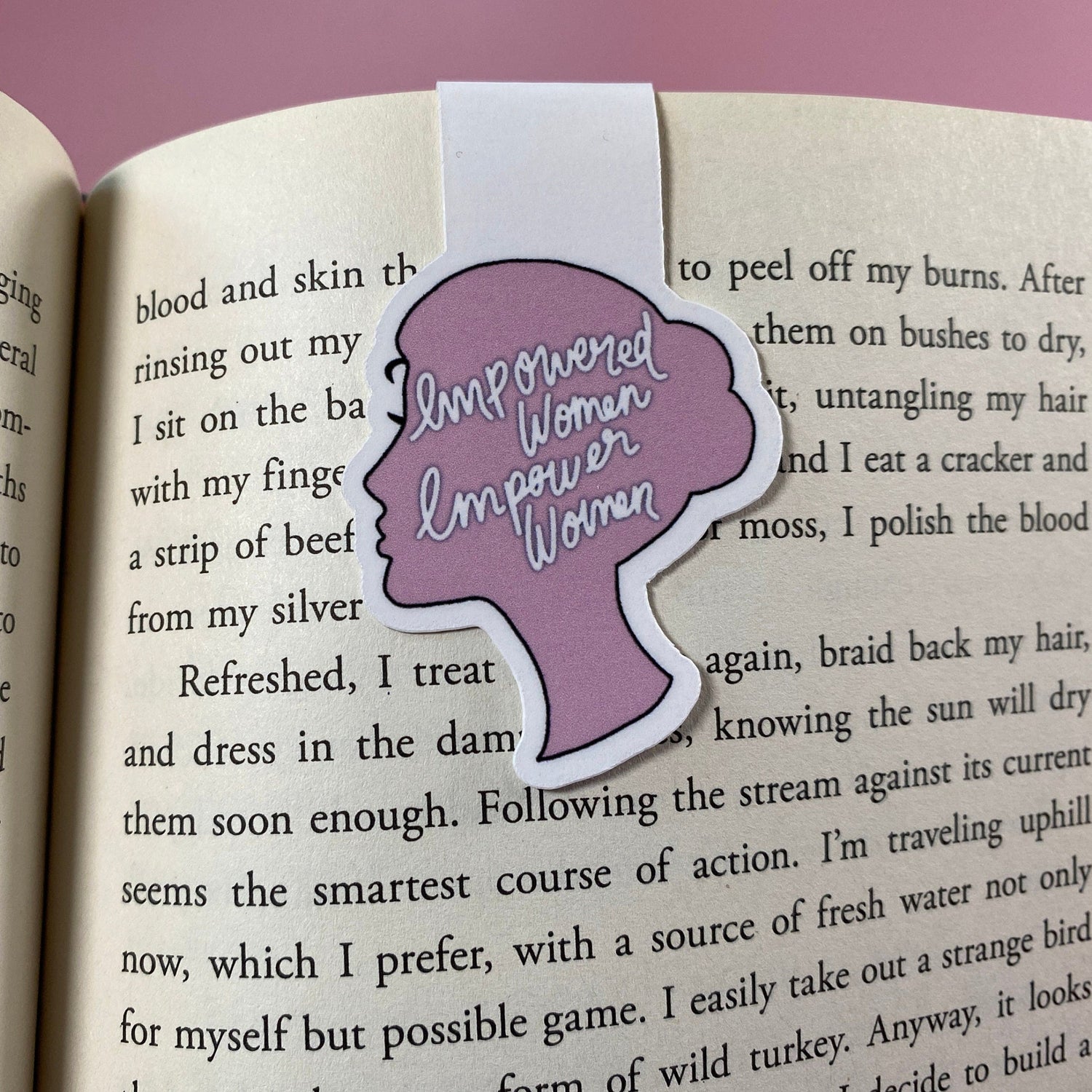 Open book with a pink bookmark featuring a woman's silhouette and text on a pink background