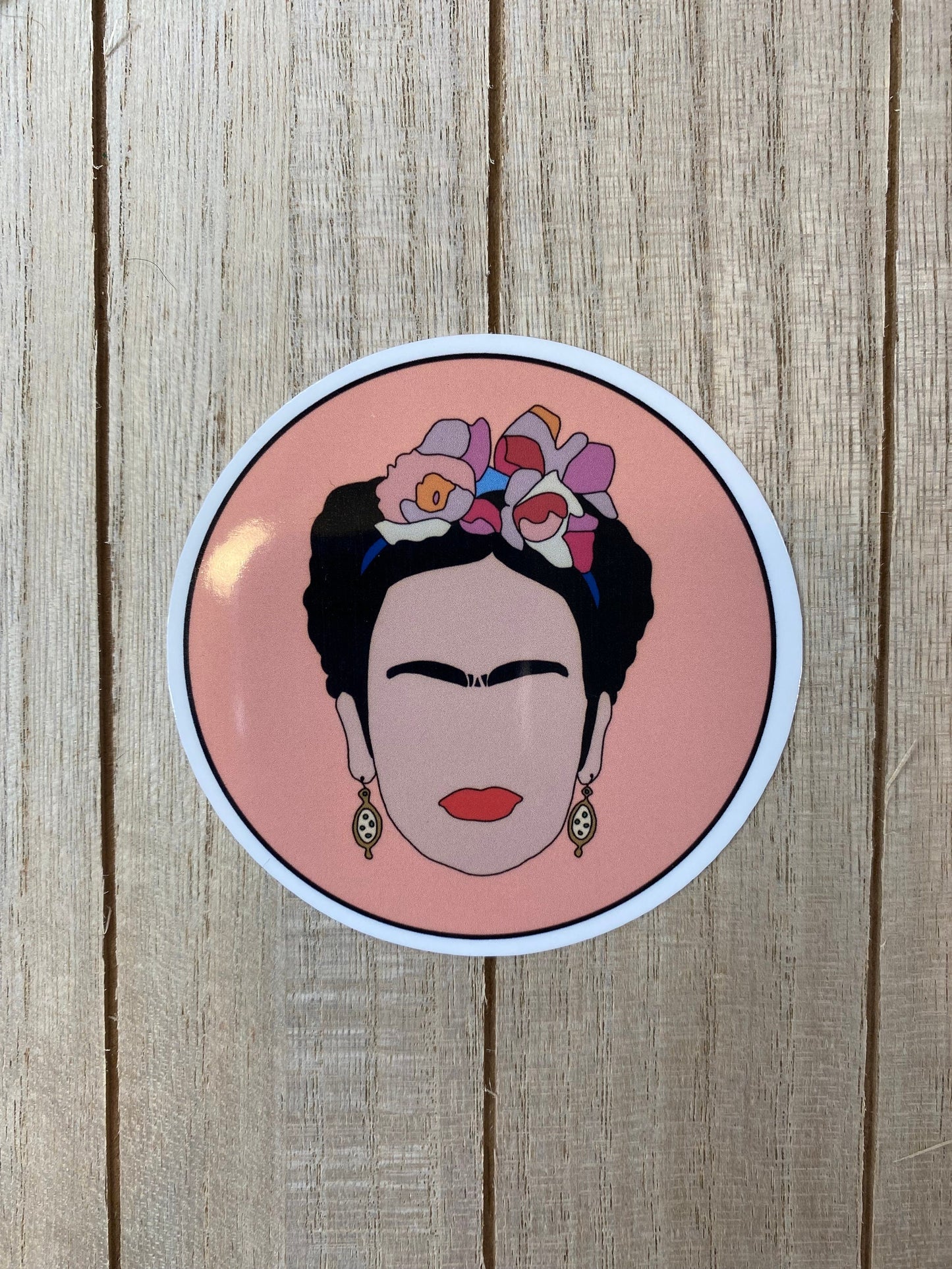 Circular sticker with Frida Kahlo with flowers in her hair on a wooden surface