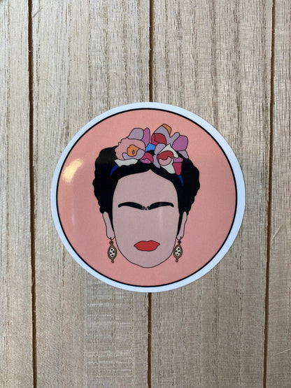 Circular sticker with Frida Kahlo with flowers in her hair on a wooden surface