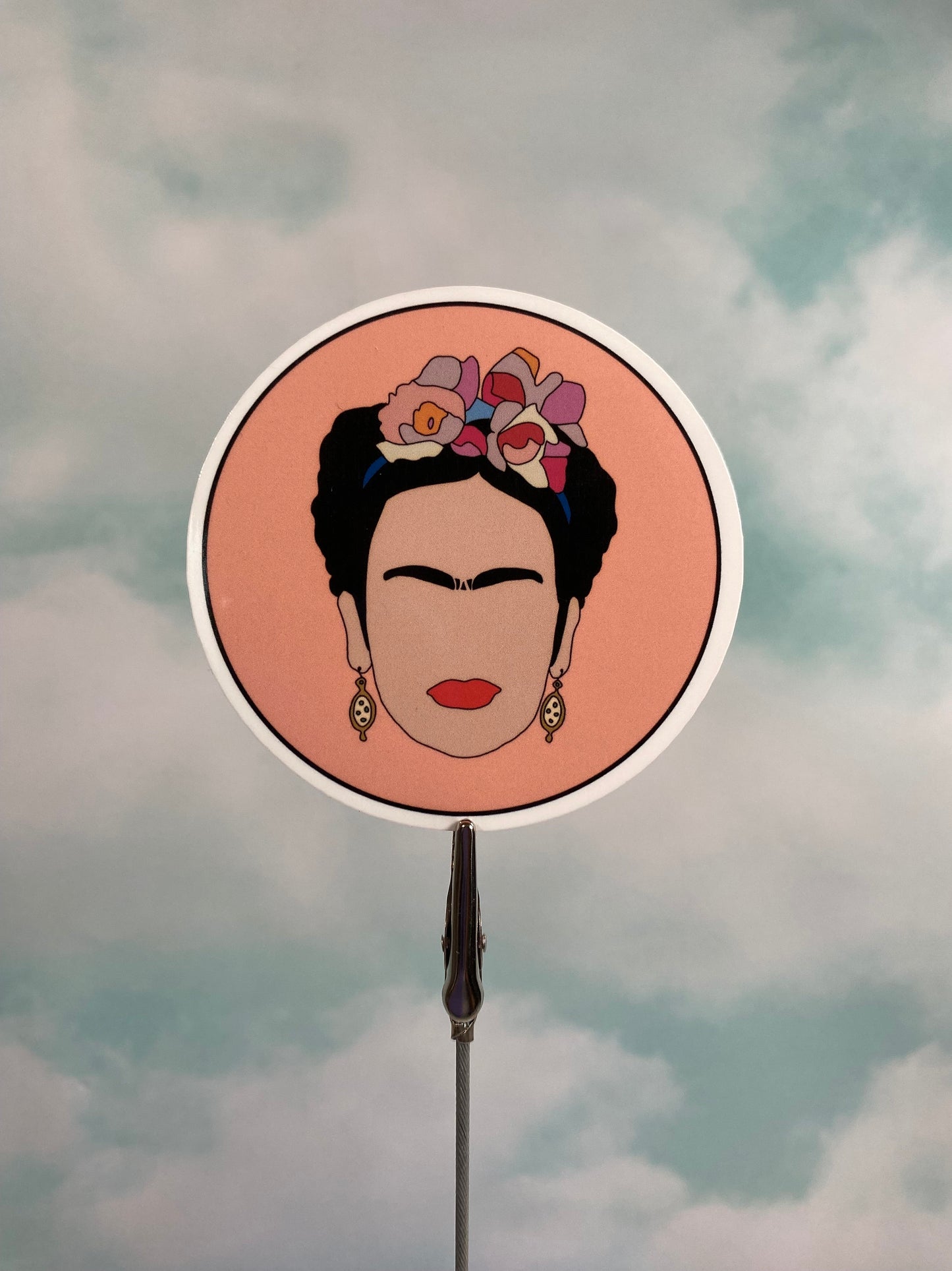 Circular mirror with a portrait of Frida Kahlo with flowers in her hair against a cloudy sky background