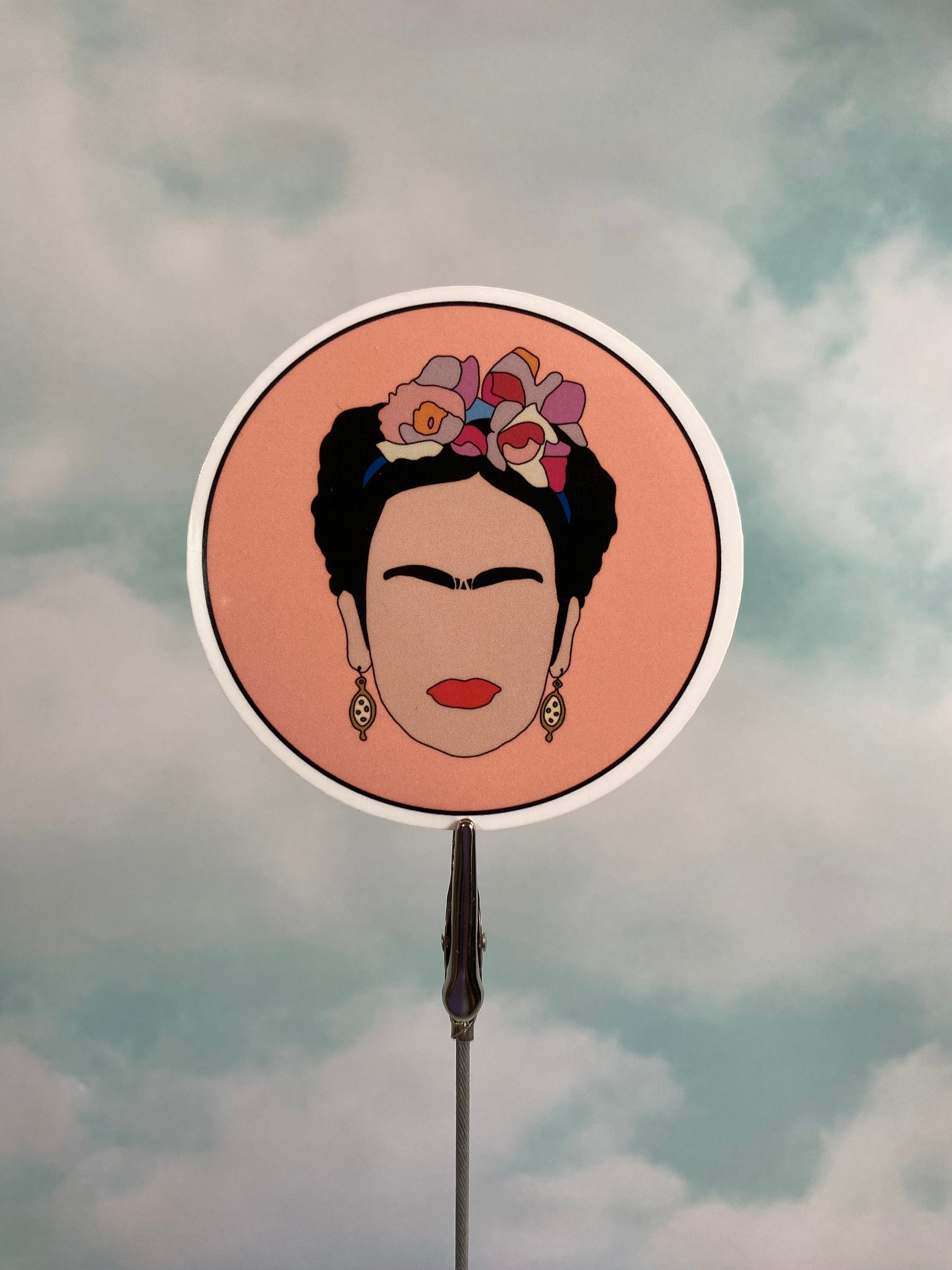 Circular mirror with a portrait of Frida Kahlo with flowers in her hair against a cloudy sky background