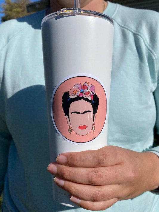 Person holding a white tumbler with a Frida Kahlo illustration on a coral orange background