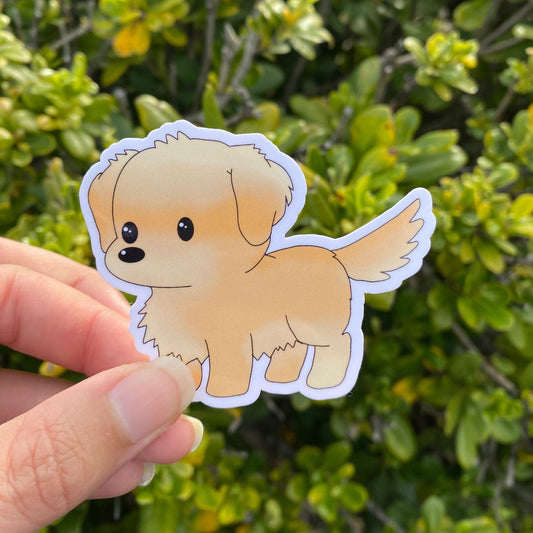 Hand holding a cartoon-style dog sticker in front of green foliage