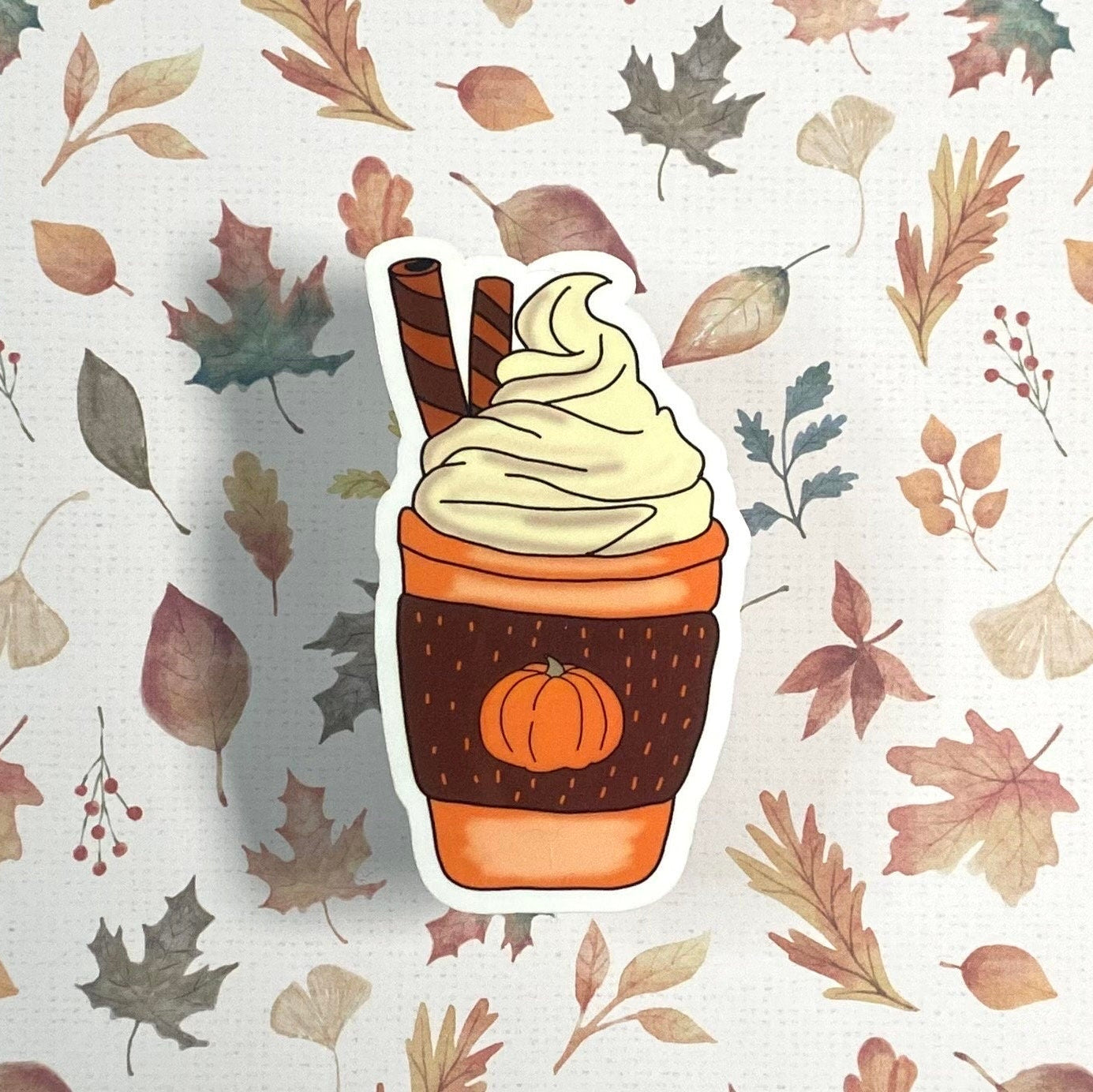Sticker of a pumpkin spice latte with whipped cream on a leaf patterned background